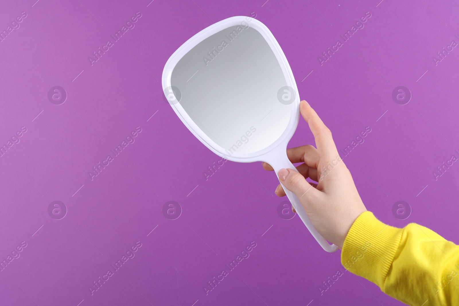 Photo of Woman holding handheld mirror on violet background, closeup. Space for text