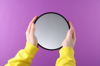 Photo of Woman holding round mirror on violet background, closeup