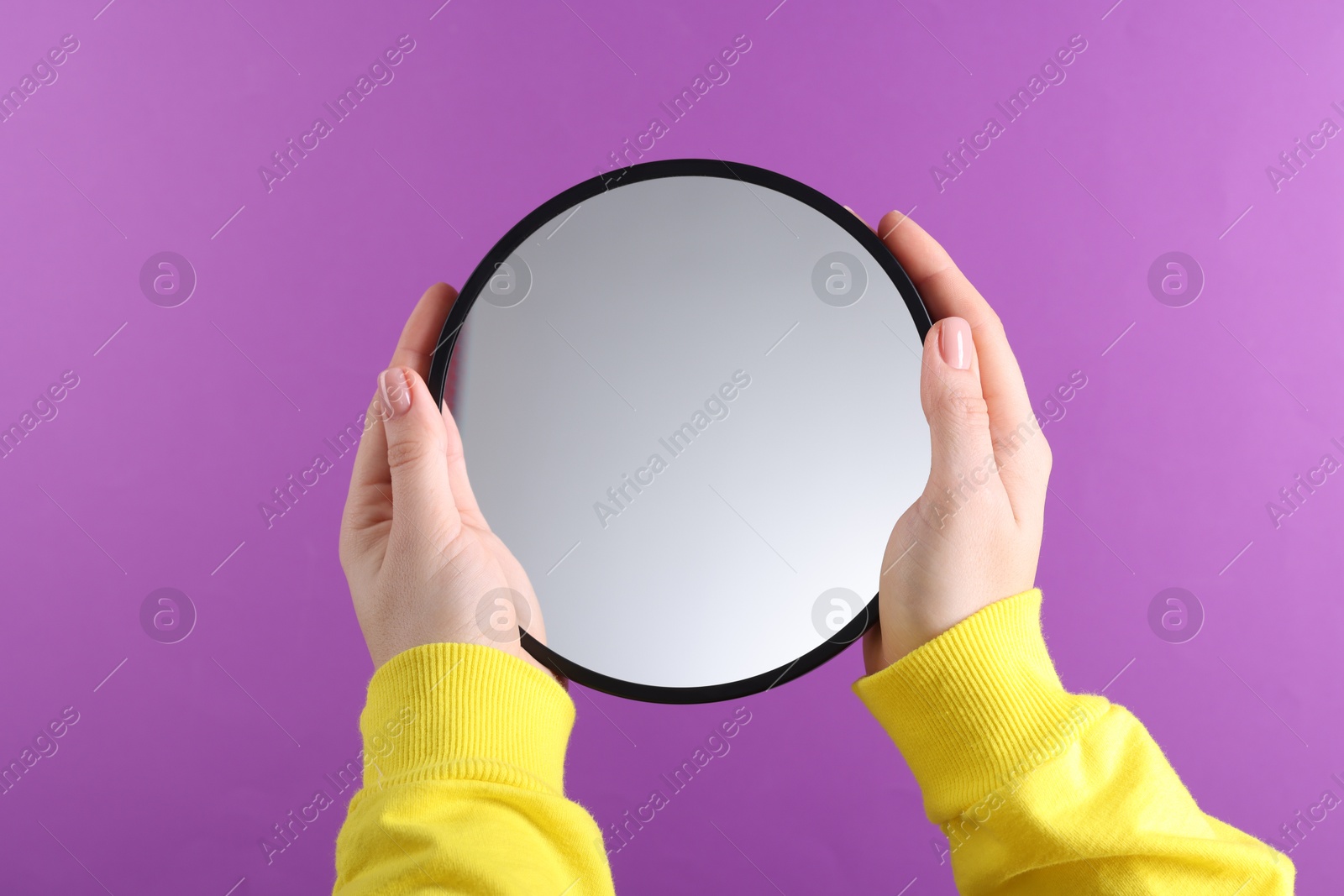 Photo of Woman holding round mirror on violet background, closeup