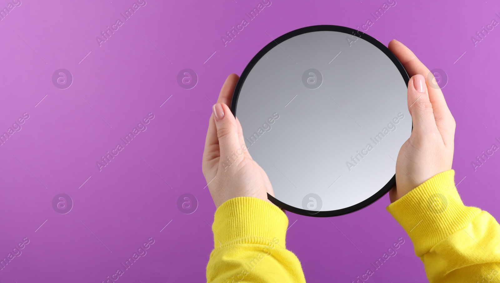 Photo of Woman holding round mirror on violet background, closeup. Space for text