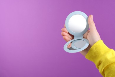 Photo of Woman holding pocket mirror on violet background, closeup. Space for text