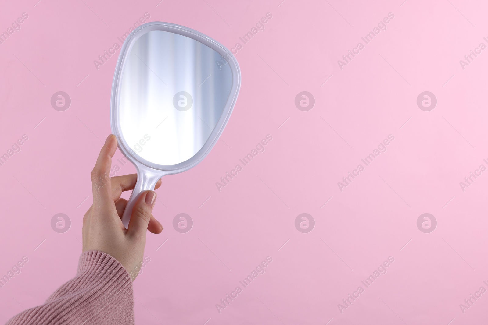 Photo of Woman holding handheld mirror on pink background, closeup. Space for text