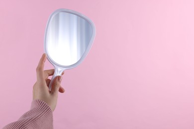 Woman holding handheld mirror on pink background, closeup. Space for text