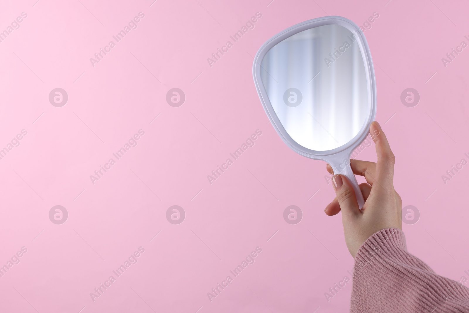 Photo of Woman holding handheld mirror on pink background, closeup. Space for text