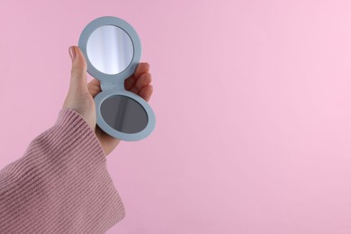 Woman holding pocket mirror on pink background, closeup. Space for text