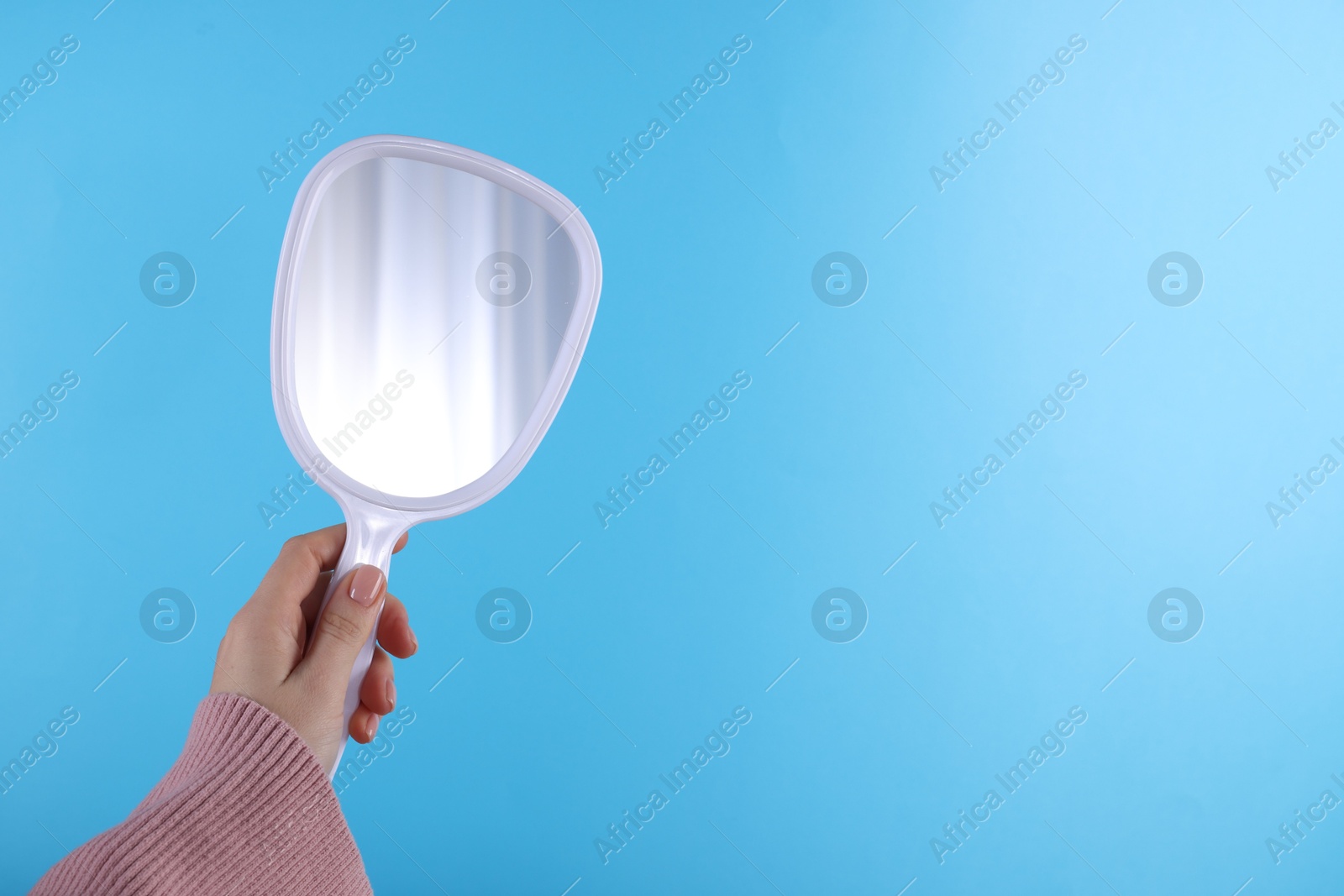 Photo of Woman holding handheld mirror on light blue background, closeup. Space for text