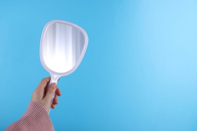 Woman holding handheld mirror on light blue background, closeup. Space for text