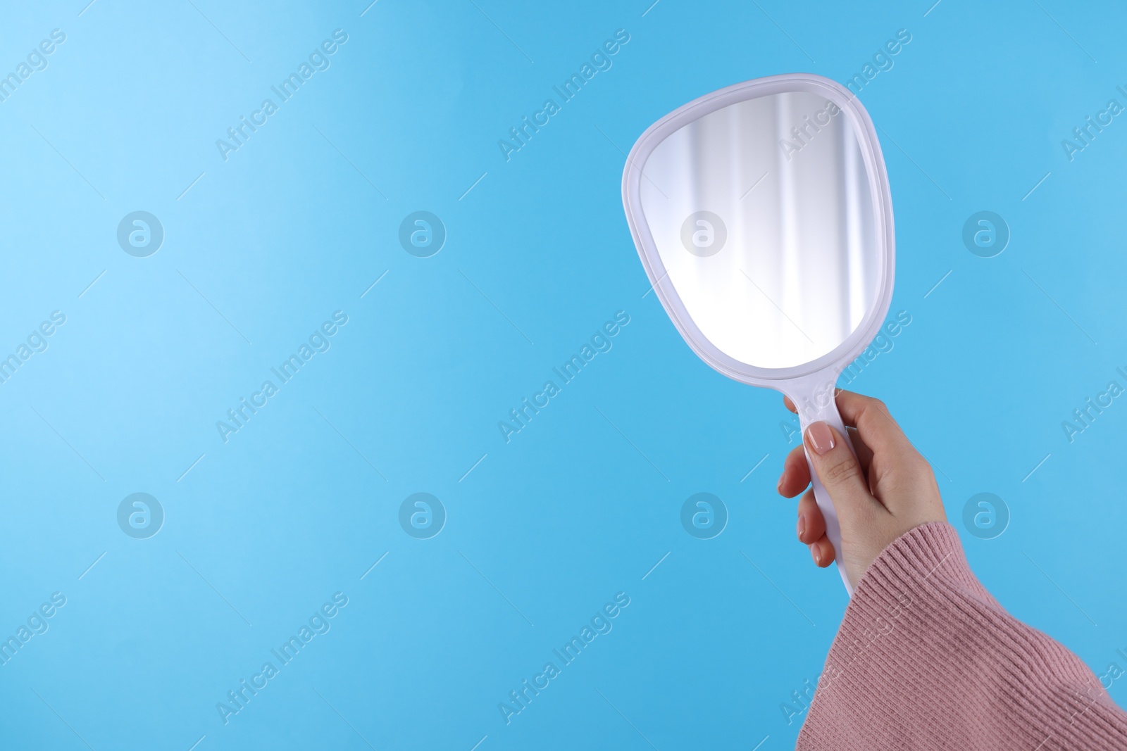 Photo of Woman holding handheld mirror on light blue background, closeup. Space for text