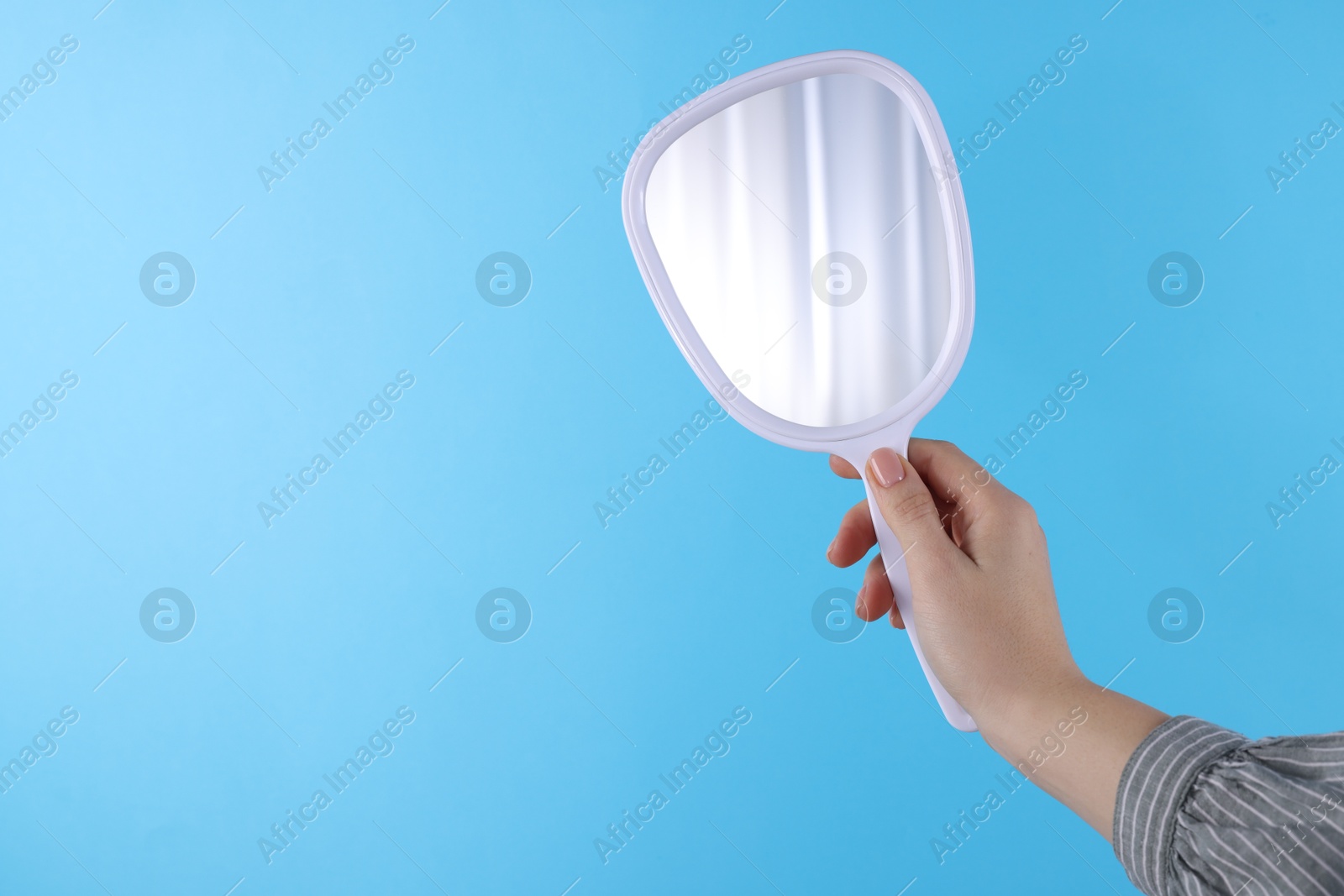 Photo of Woman holding handheld mirror on light blue background, closeup. Space for text