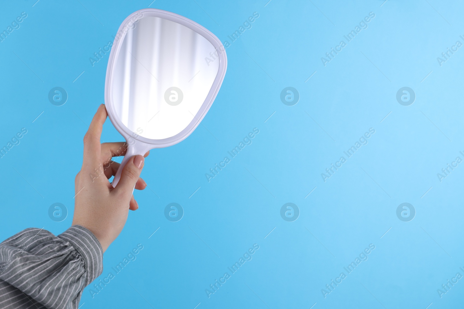 Photo of Woman holding handheld mirror on light blue background, closeup. Space for text