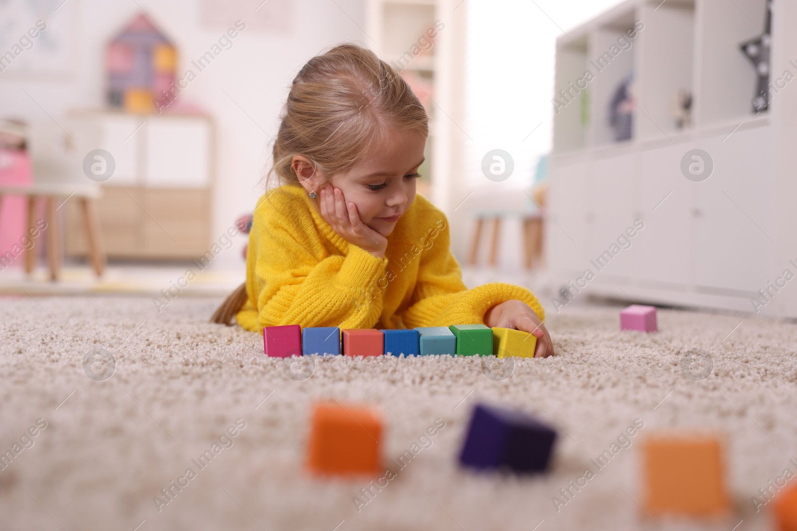 Photo of Cute girl playing with colorful cubes on carpet at home