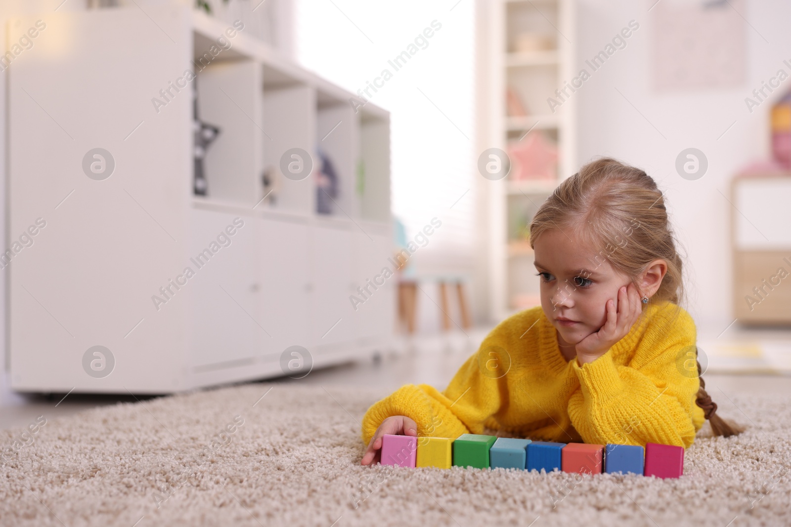 Photo of Cute girl with colorful cubes on carpet at home. Space for text