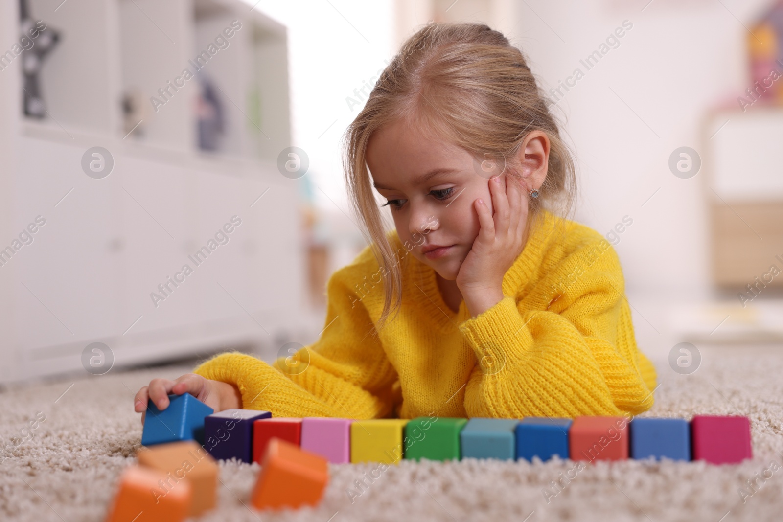 Photo of Cute girl playing with colorful cubes on carpet at home