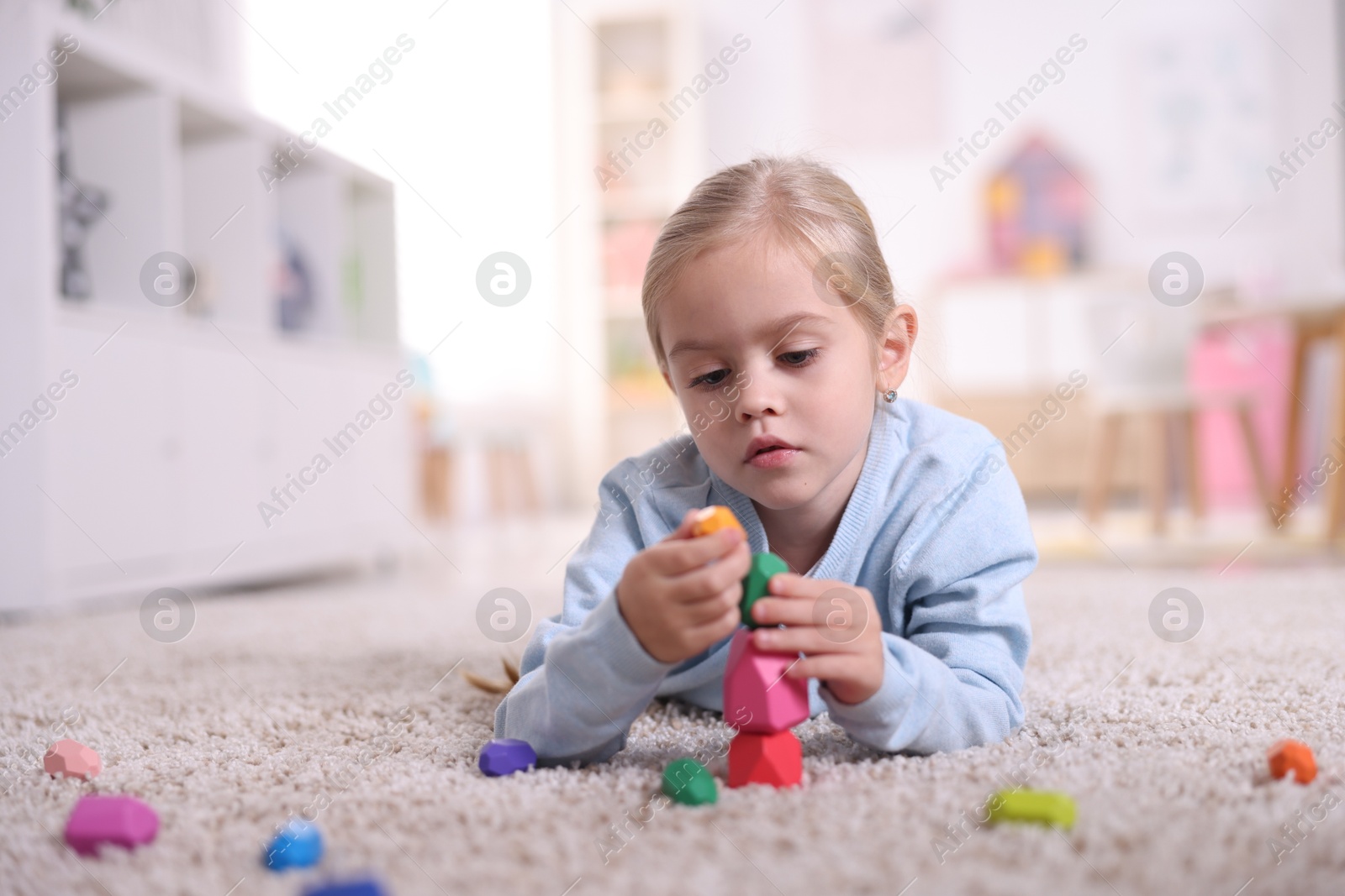 Photo of Cute girl building tower with balancing stones on carpet at home. Space for text