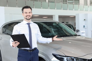 Photo of Happy salesman near new silver car in salon