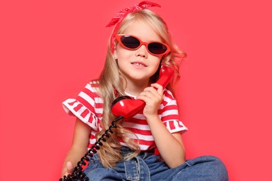 Cute little girl with handset of telephone on red background