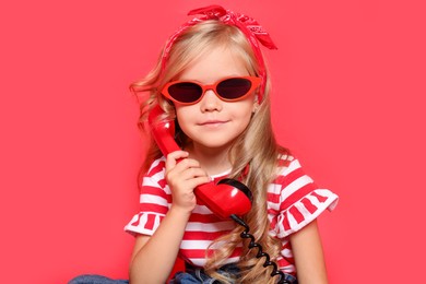 Cute little girl with handset of telephone on red background