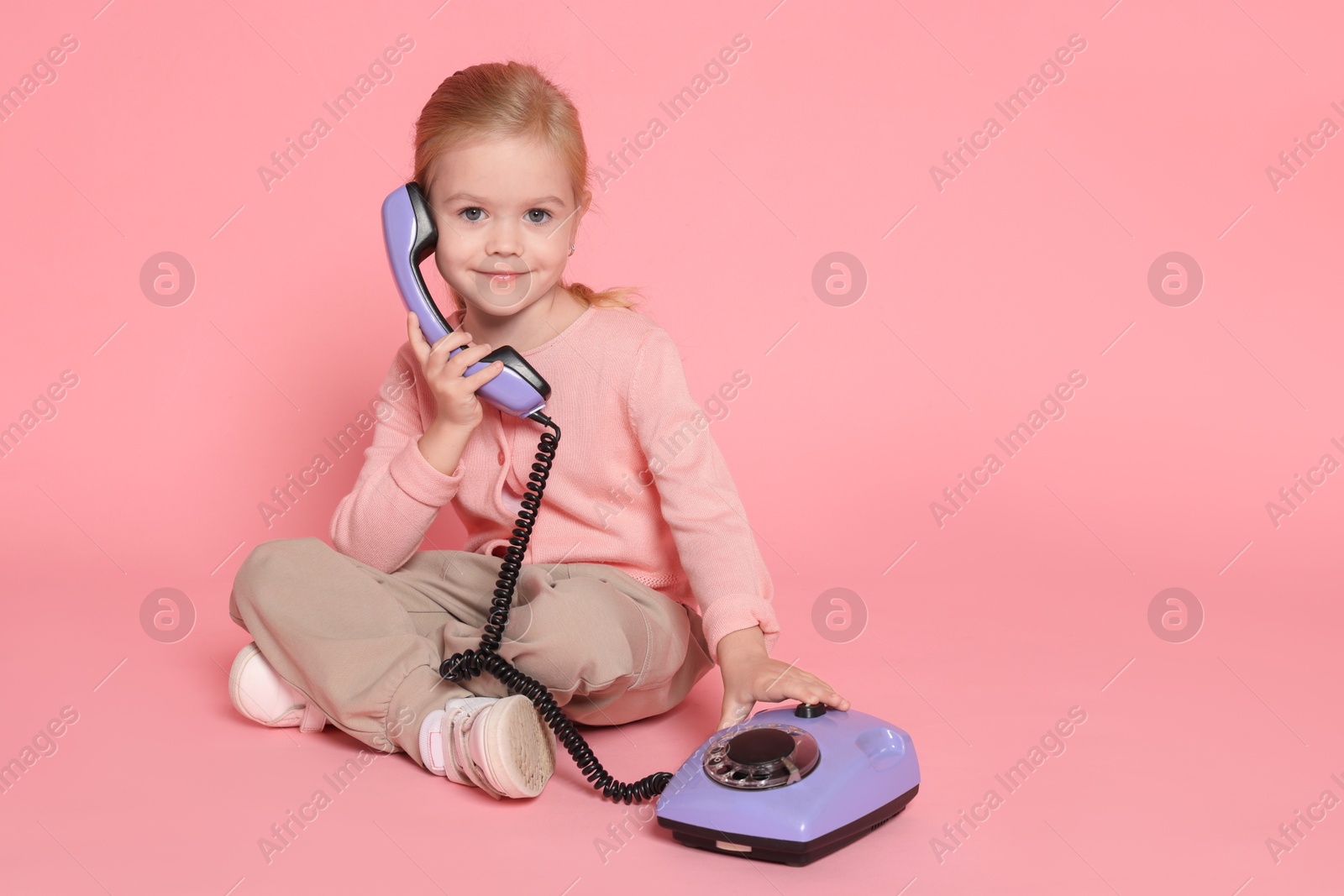 Photo of Cute little girl with telephone on pink background, space for text