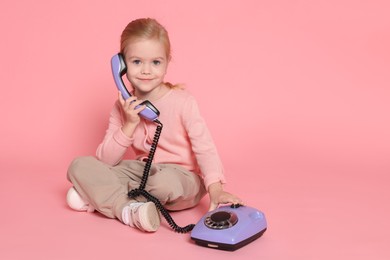 Photo of Cute little girl with telephone on pink background, space for text