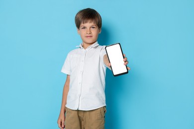 Cute little boy with smartphone on light blue background