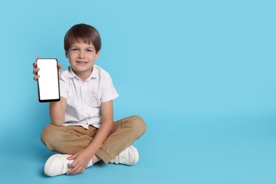 Cute little boy with smartphone on light blue background, space for text