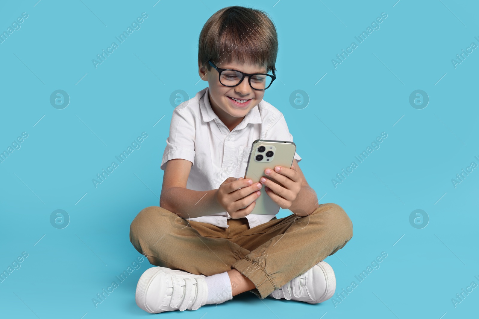 Photo of Cute little boy with smartphone on light blue background