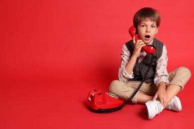 Photo of Cute little boy with old telephone on red background, space for text