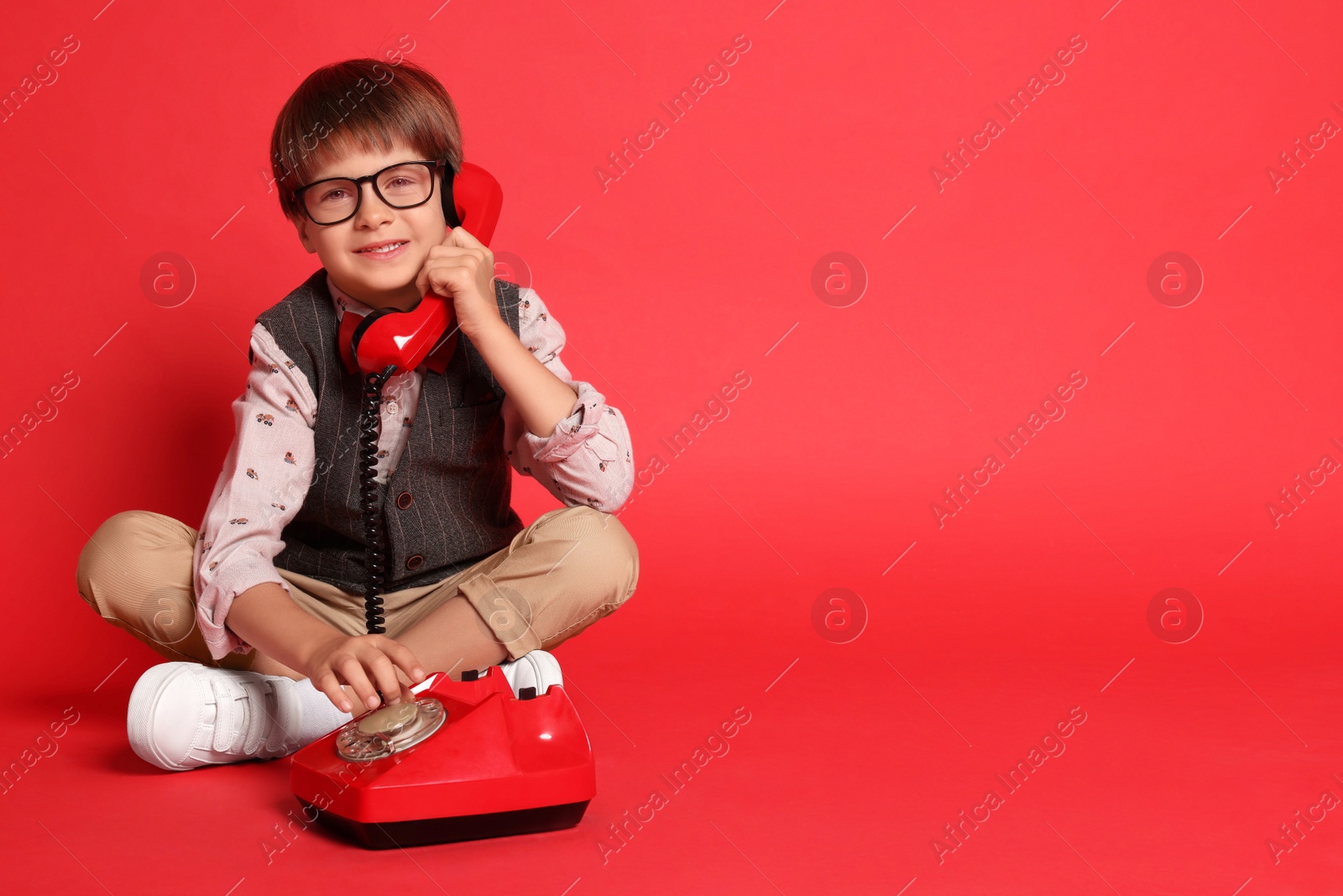 Photo of Cute little boy with old telephone on red background, space for text