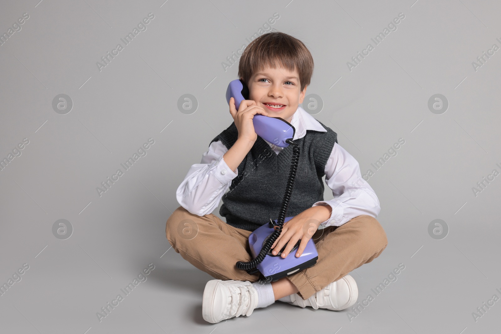 Photo of Cute little boy with old telephone on grey background