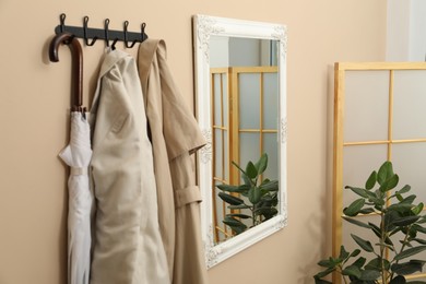 Photo of Coat rack with clothes, mirror, houseplant and folding screen in hallway. Interior design