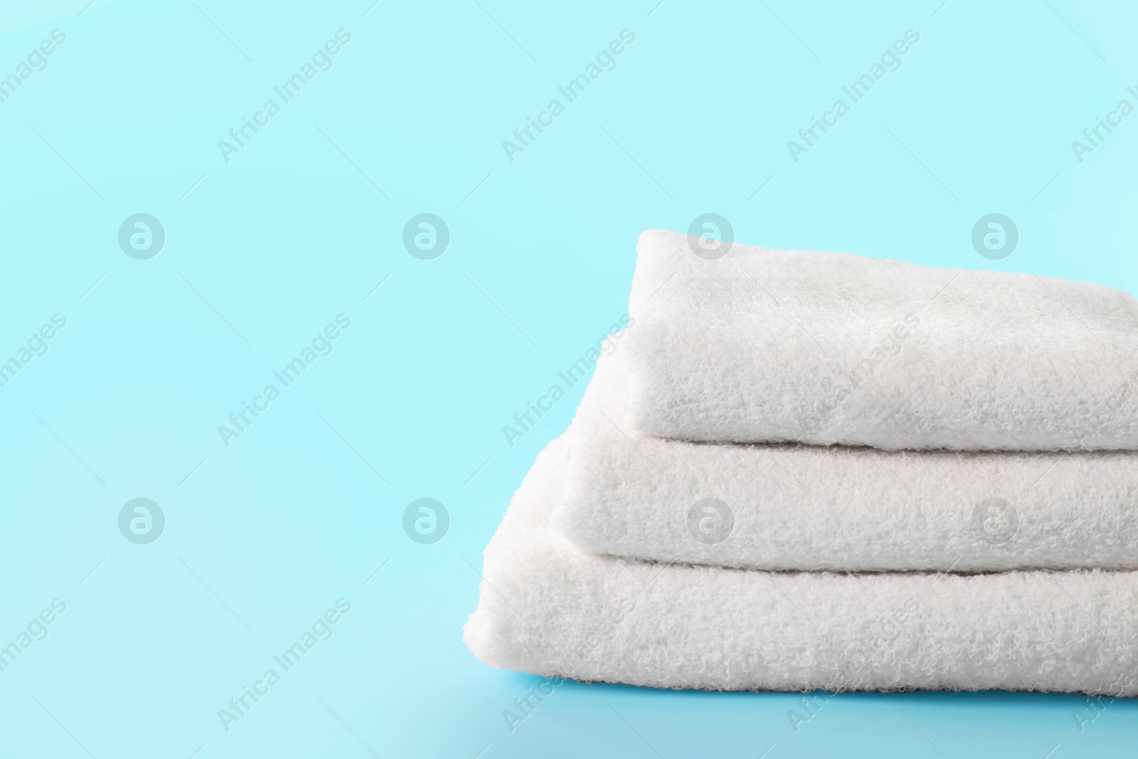 Photo of Stacked clean terry towels on light blue background, space for text