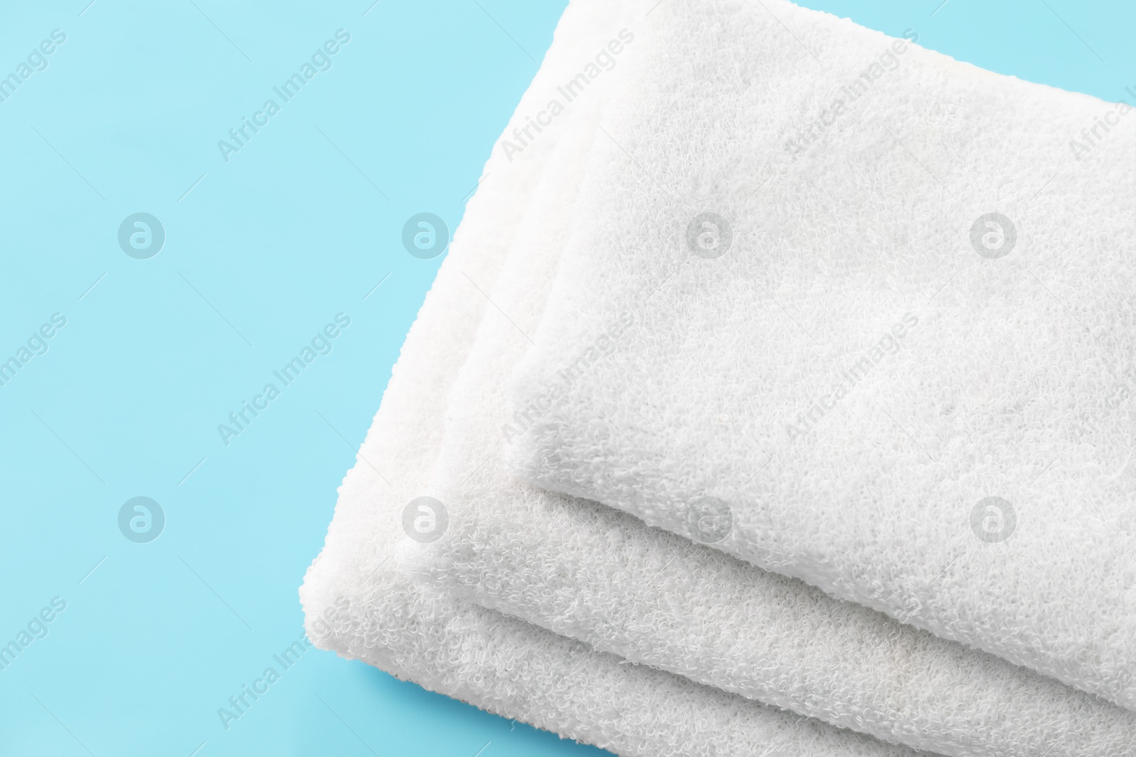 Photo of Stacked clean terry towels on light blue background, closeup. Space for text