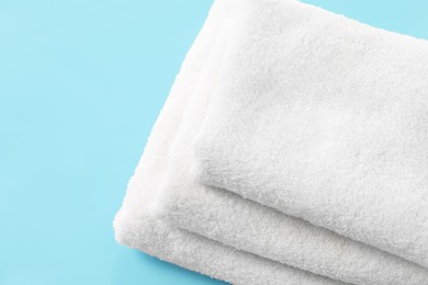 Photo of Stacked clean terry towels on light blue background, closeup. Space for text