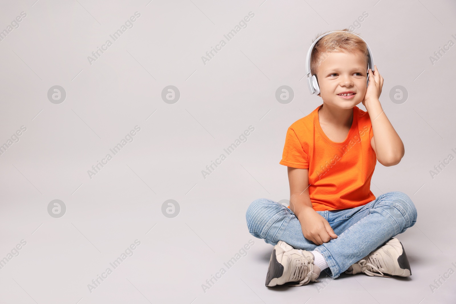 Photo of Little boy listening to music on light grey background, space for text