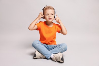 Little boy listening to music on light grey background