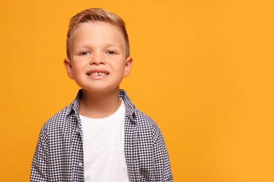 Portrait of little boy with stylish clothes on orange background, space for text