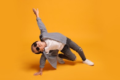 Photo of Little boy with stylish clothes and sunglasses on orange background