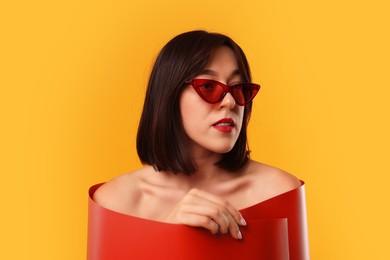 Photo of Beautiful young woman with sunglasses posing on orange background