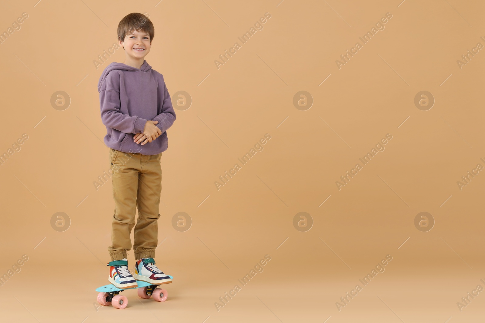 Photo of Little boy with skateboard on beige background, space for text