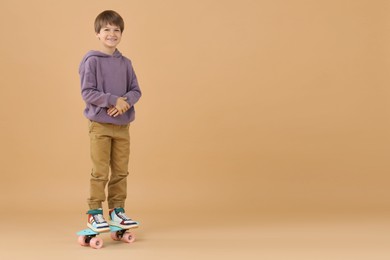 Little boy with skateboard on beige background, space for text