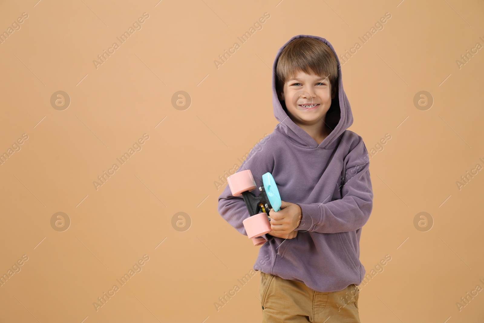 Photo of Little boy with skateboard on beige background, space for text