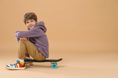 Little boy with skateboard on beige background, space for text