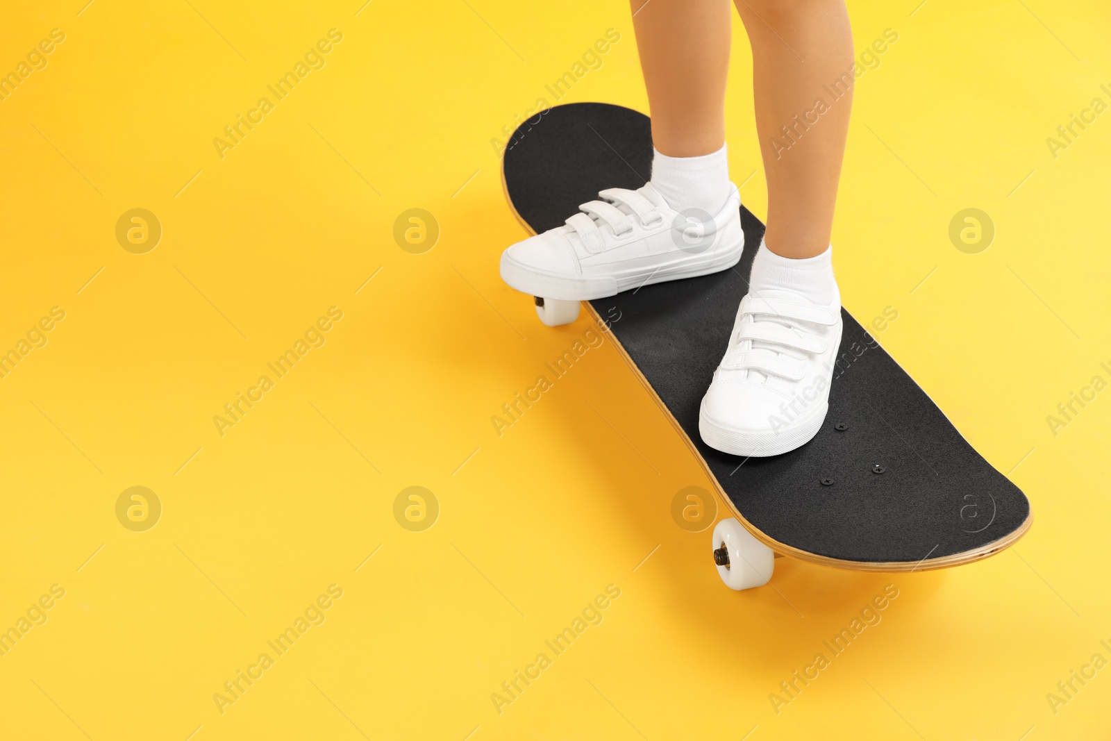 Photo of Little boy with skateboard on yellow background, closeup. Space for text