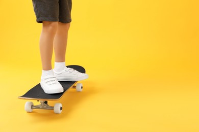 Photo of Little boy with skateboard on yellow background, closeup. Space for text