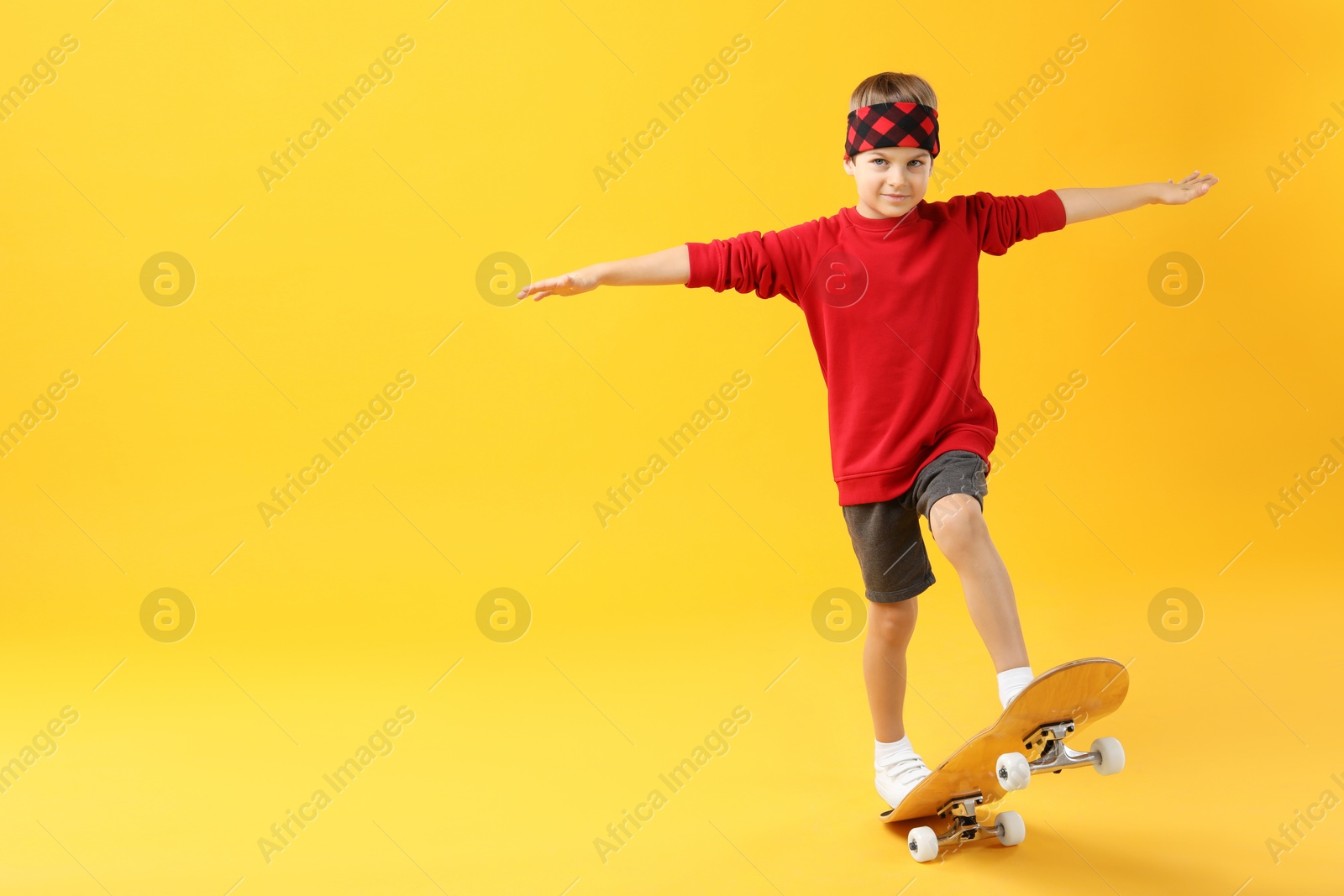 Photo of Little boy with skateboard on yellow background, space for text