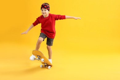 Little boy with skateboard on yellow background, space for text