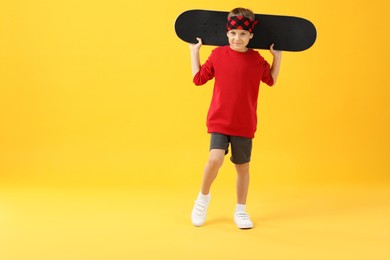 Little boy with skateboard on yellow background, space for text