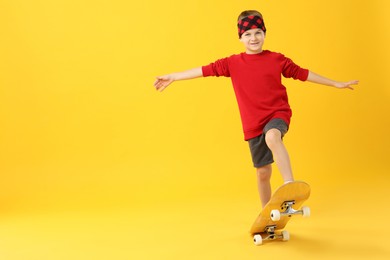 Little boy with skateboard on yellow background, space for text