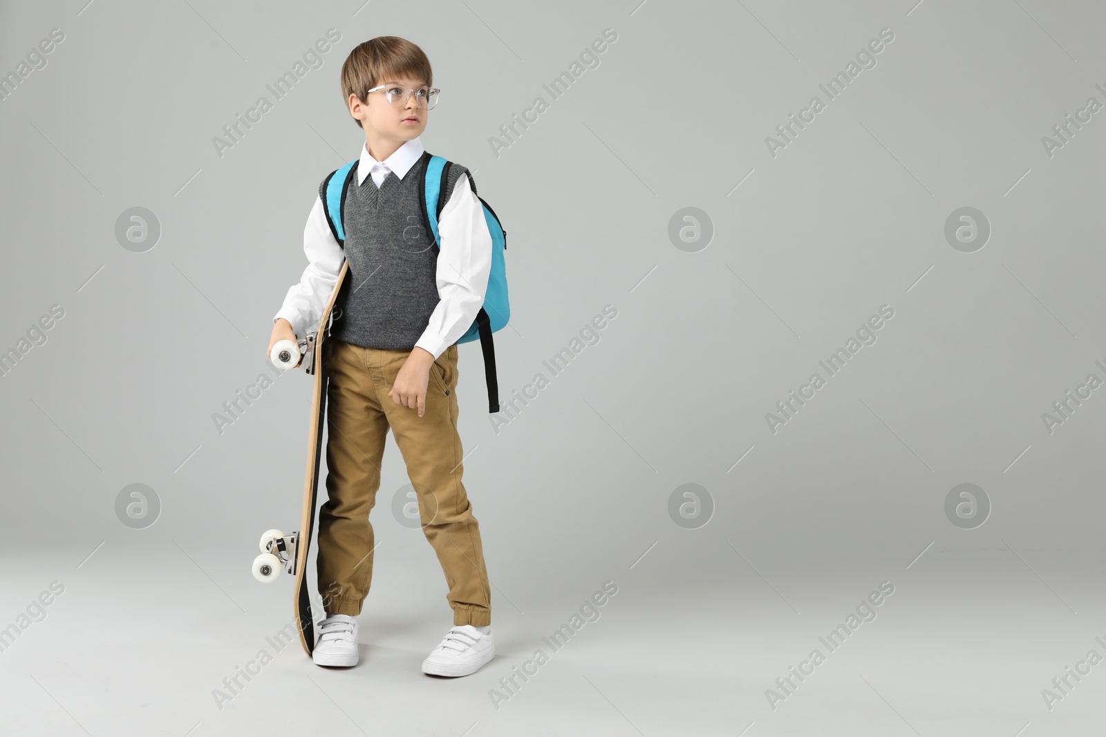 Photo of Little boy with skateboard on light grey background, space for text