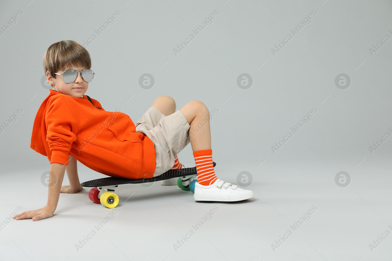 Photo of Little boy with skateboard on light grey background, space for text